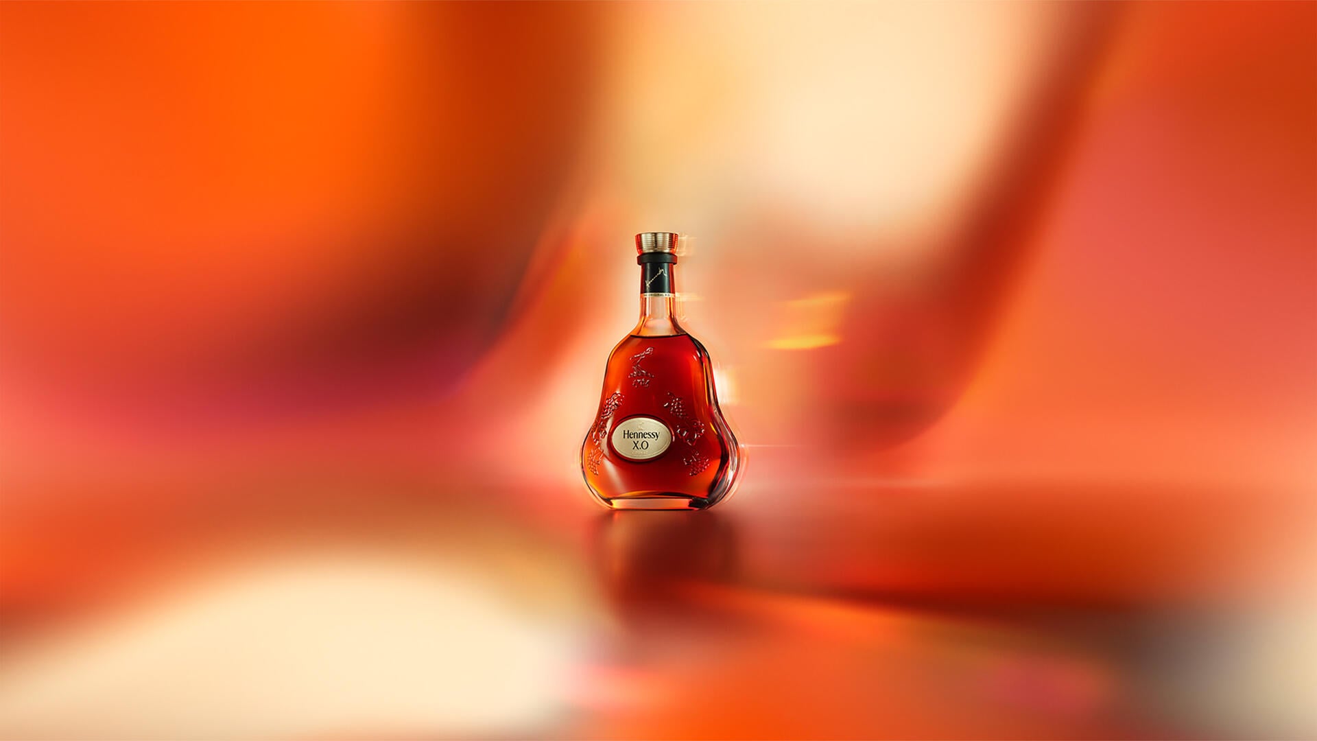 A bottle of Hennessy X.O cognac, set against an artistic red-orange background