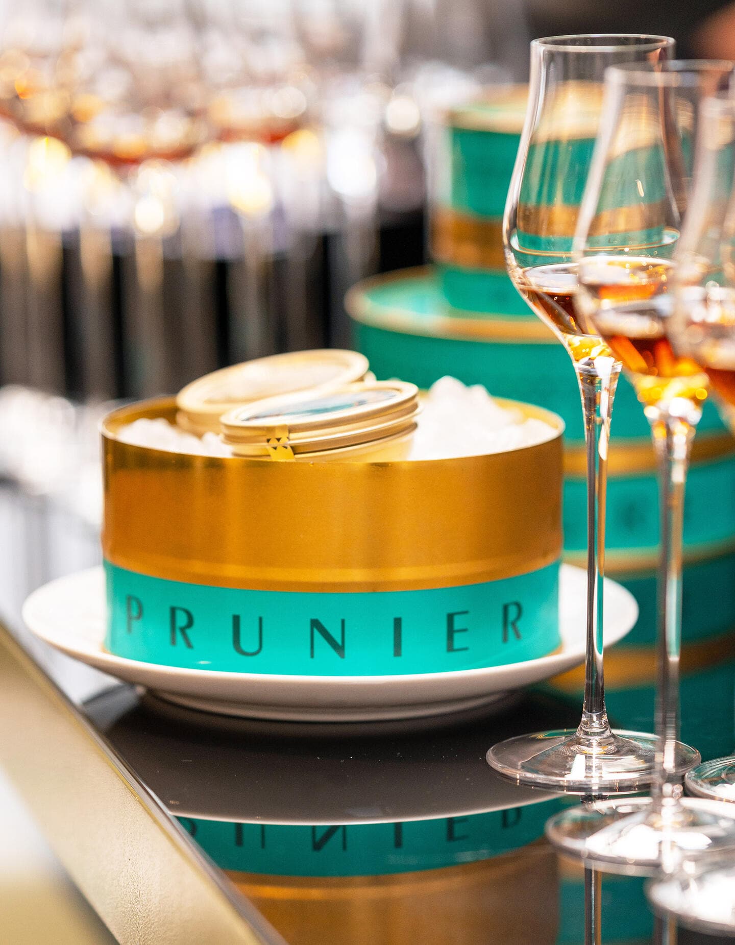 Turquoise tin of Prunier Oscietra Caviar, next to glasses of Hennessy cognac