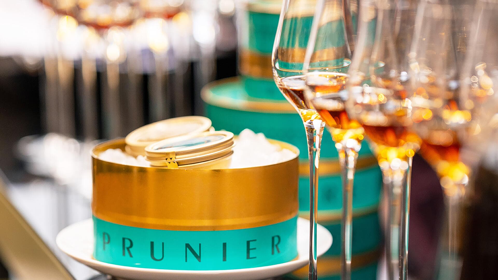 Boite de caviar Prunier turquoise et doré, à côté de verres de cognac Hennessy