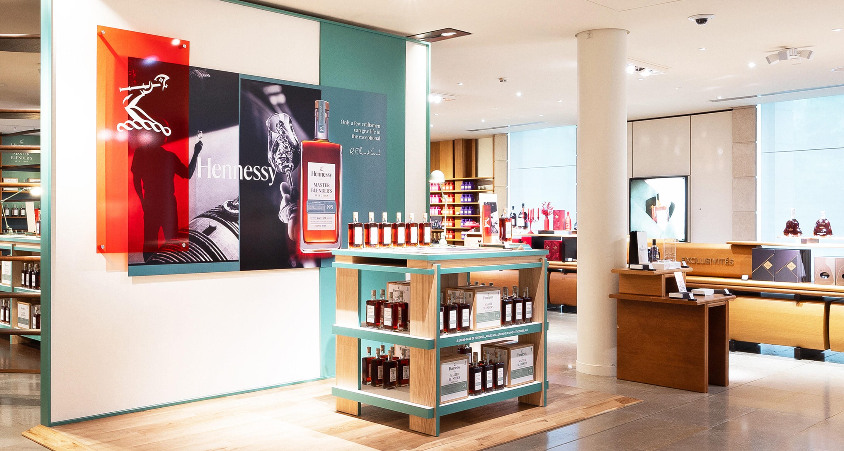 Vue intérieure de la boutique Hennessy de Cognac baignée de lumière naturelle, montrant des étagères colorées sur lesquelles sont exposées plusieurs carafes différentes de la collection Hennessy