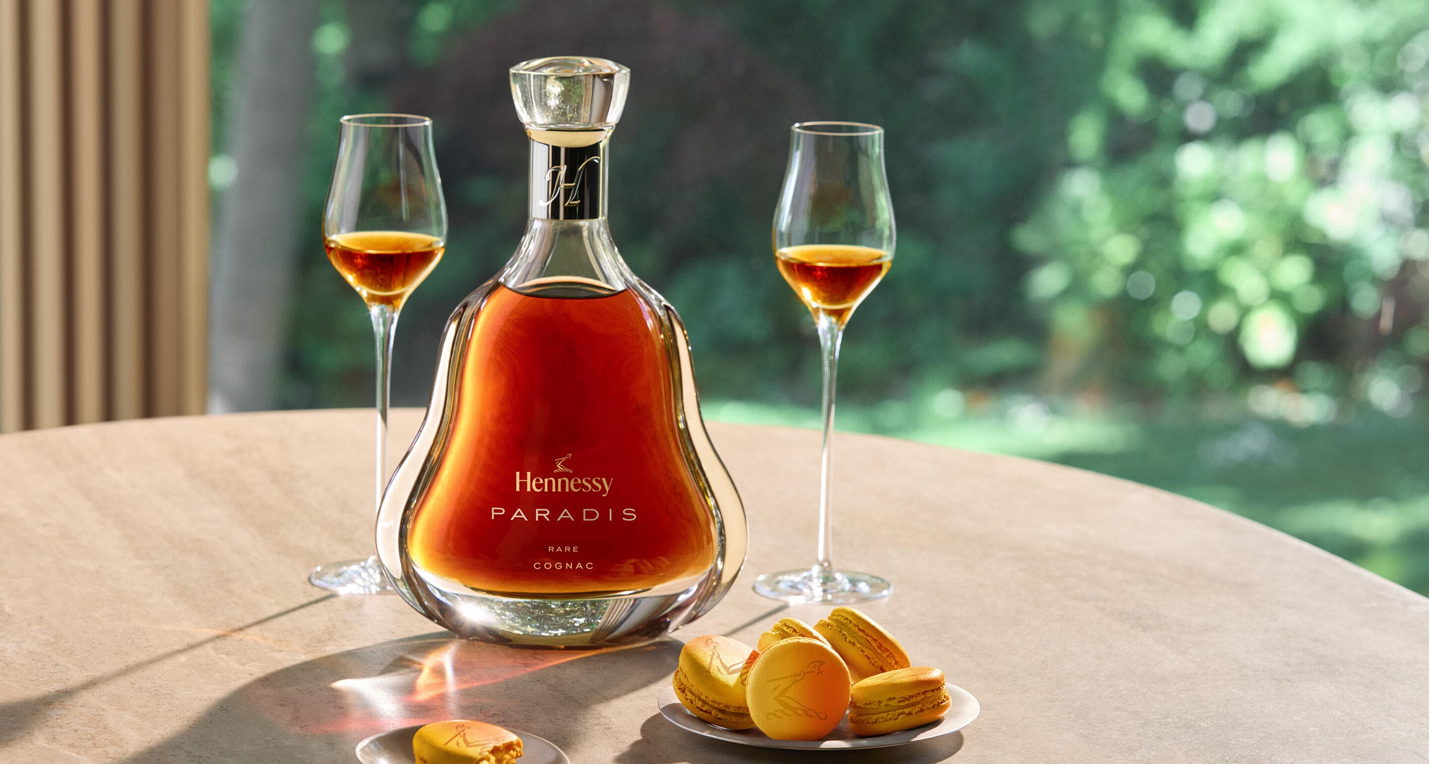 Carafe de Hennessy Paradis upgrade posée sur une table, à côté de 2 verres de cognac et d'une assiette de macarons au fruit de la passion