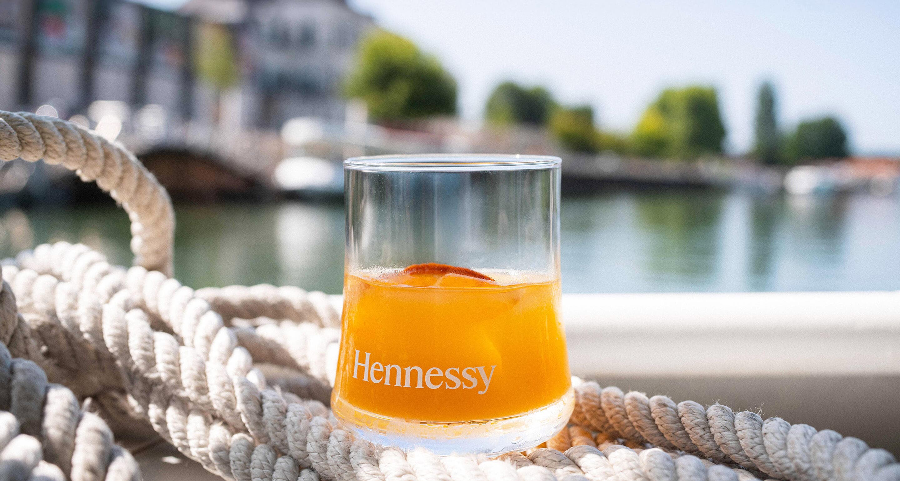 Un verre de cocktail au cognac Hennessy est posé sur un bateau, lors d'une traversée de la Charente, avec le bâtiment des Visites Hennessy en arrière-plan