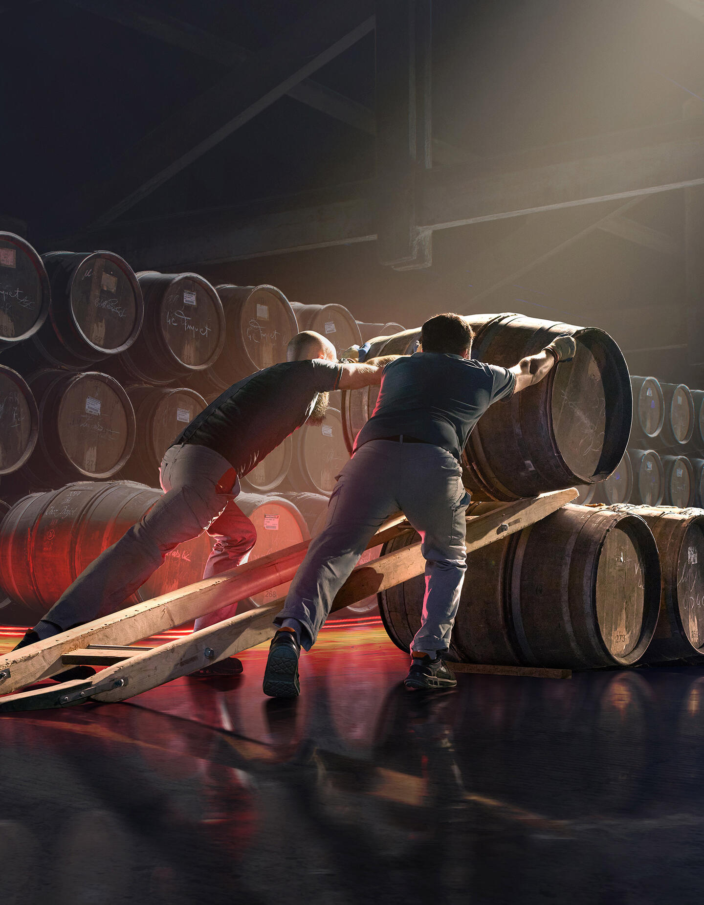 Deux agents de chais Hennessy roulent des barriques et les alignent dans des chais de vieillissement