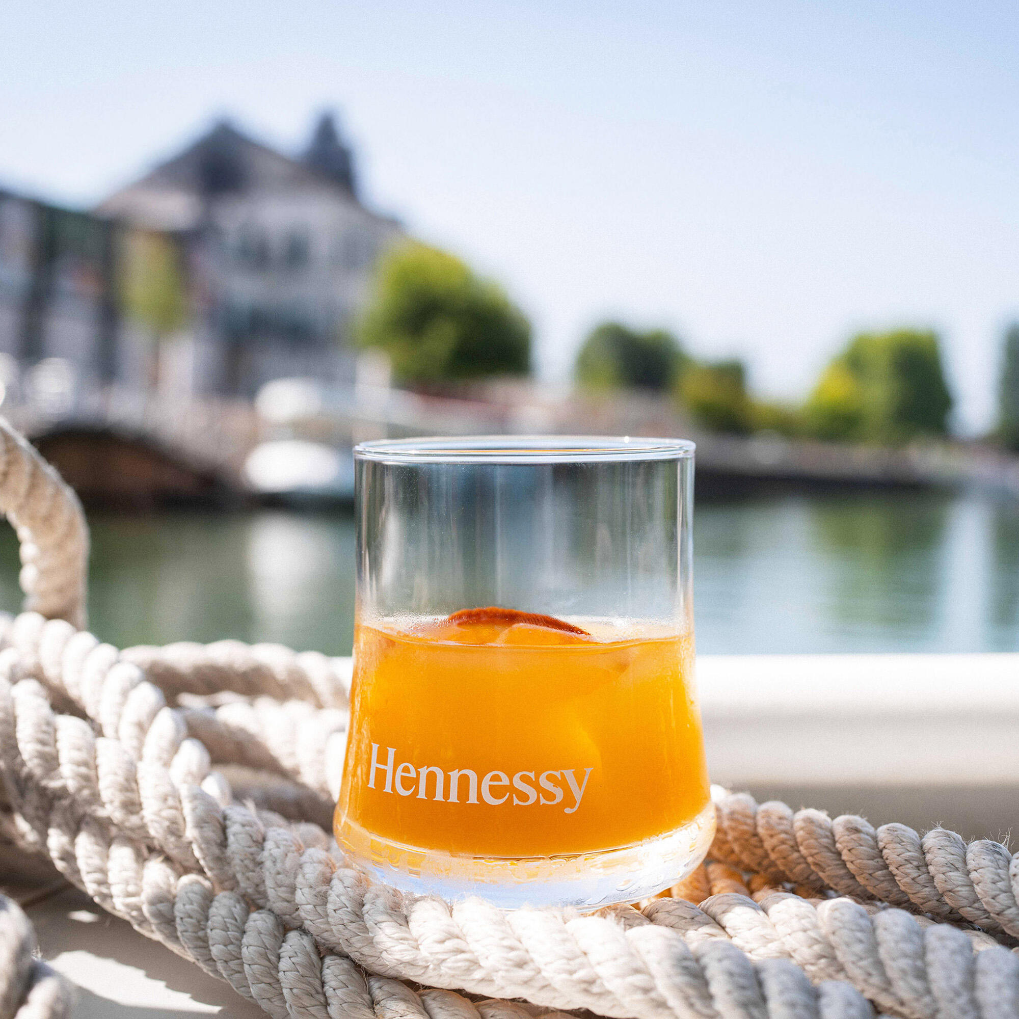 Verre de cocktail au Hennessy VSOP servi sur un bateau, à Cognac, avec en arrière-plan, les quais Hennessy et le bâtiment des Visites Hennessy