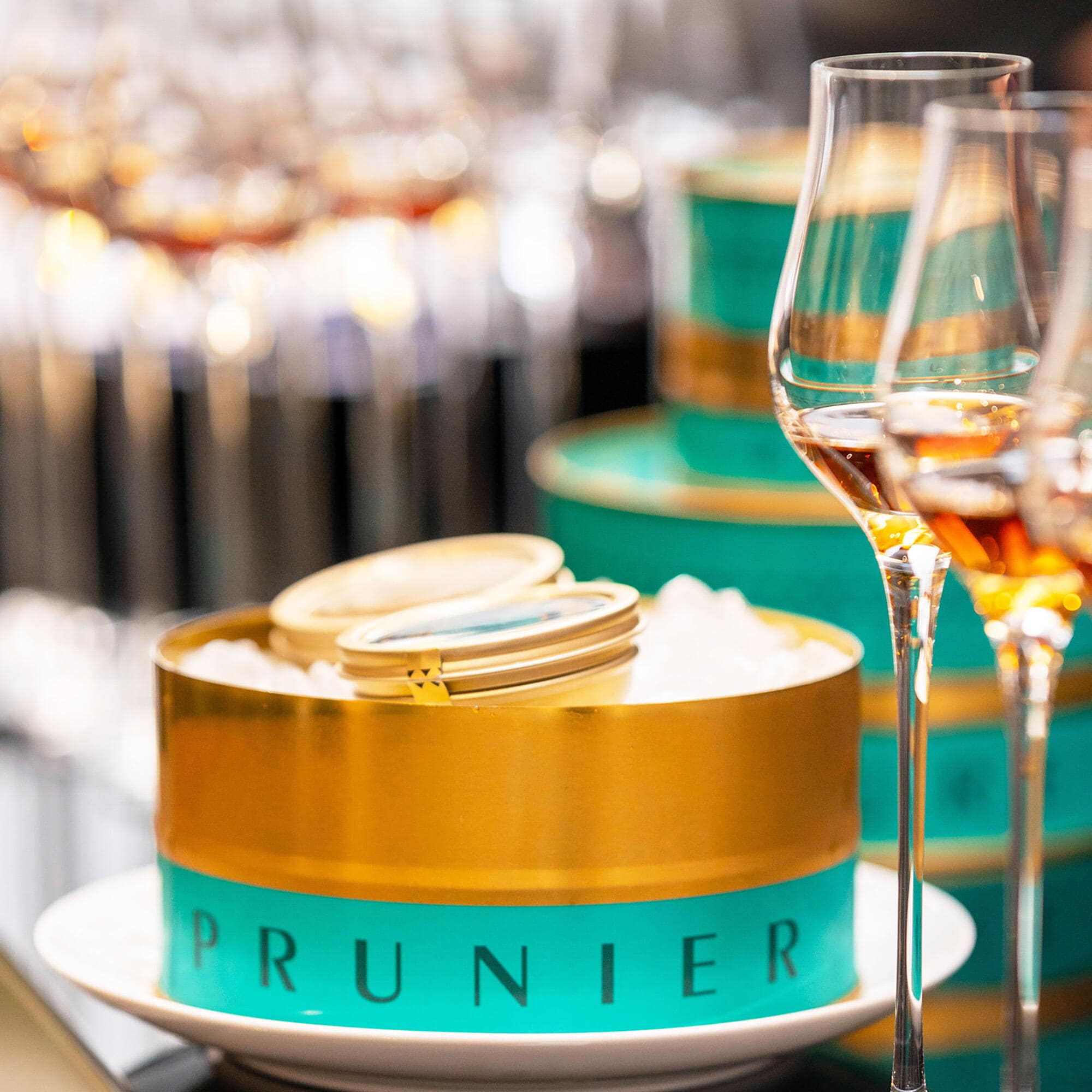 Boite or et turquoise de caviar osciètre Prunier, à côté de 2 verres de cognac Hennessy Paradis