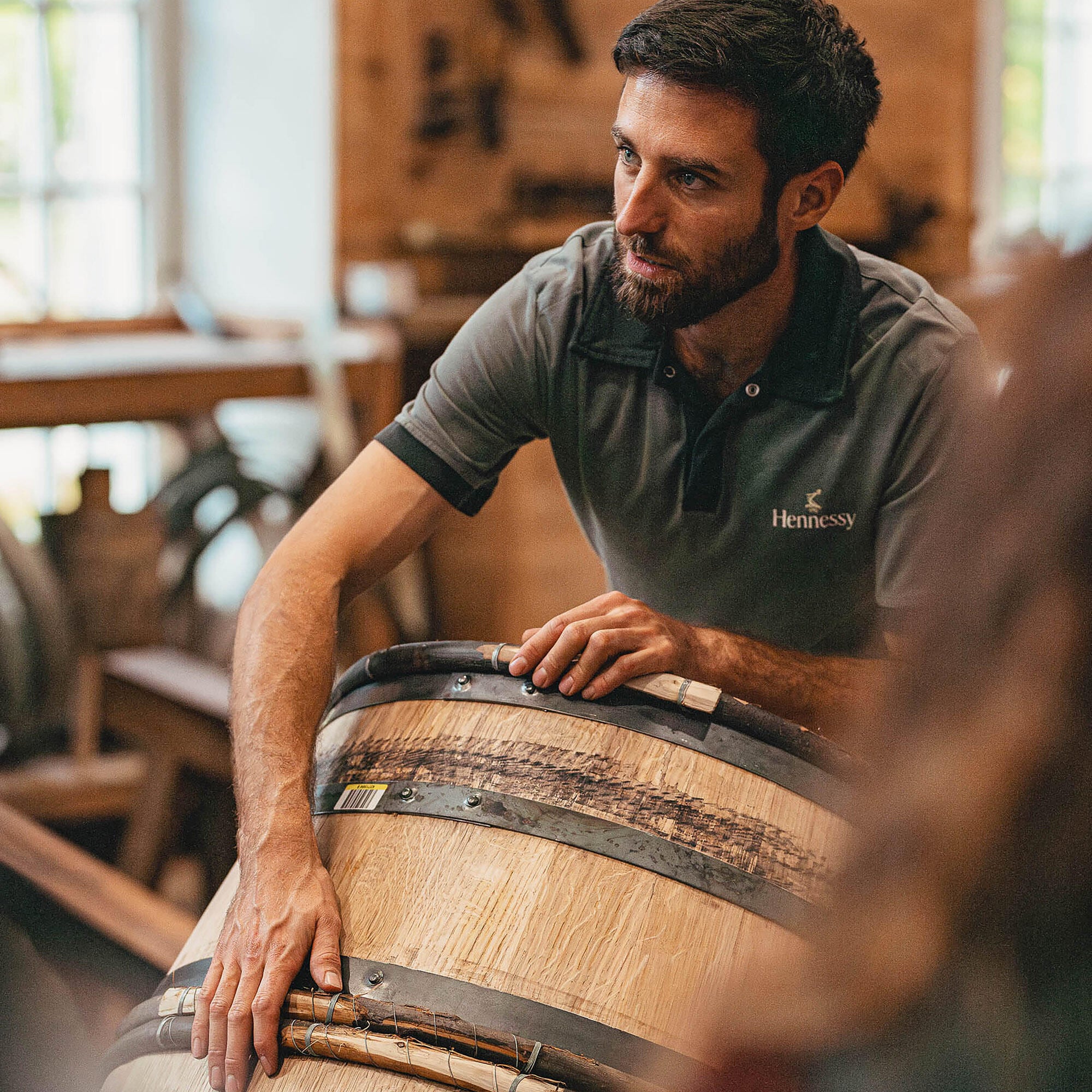 Artisan tonnelier de la Maison Hennessy, expliquant son métier, les mains posées sur une barrique de chêne