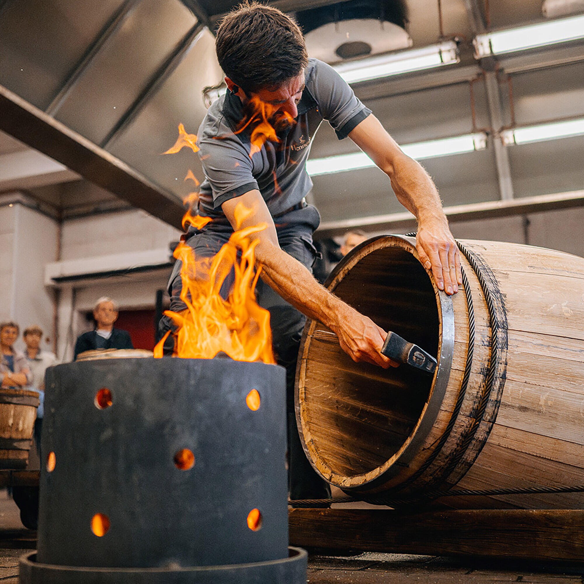 Un artisan tonnelier Hennessy finalise la création d'une barrique à l'aide de son marteau, après que la barrique ait été chauffée à haute température par le feu