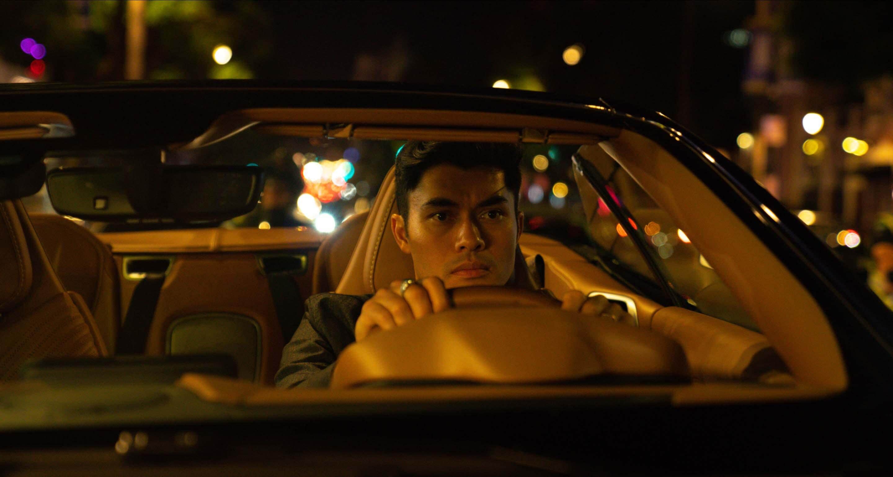 Henry Golding driving through the neon-lit streets of Los Angeles at night.