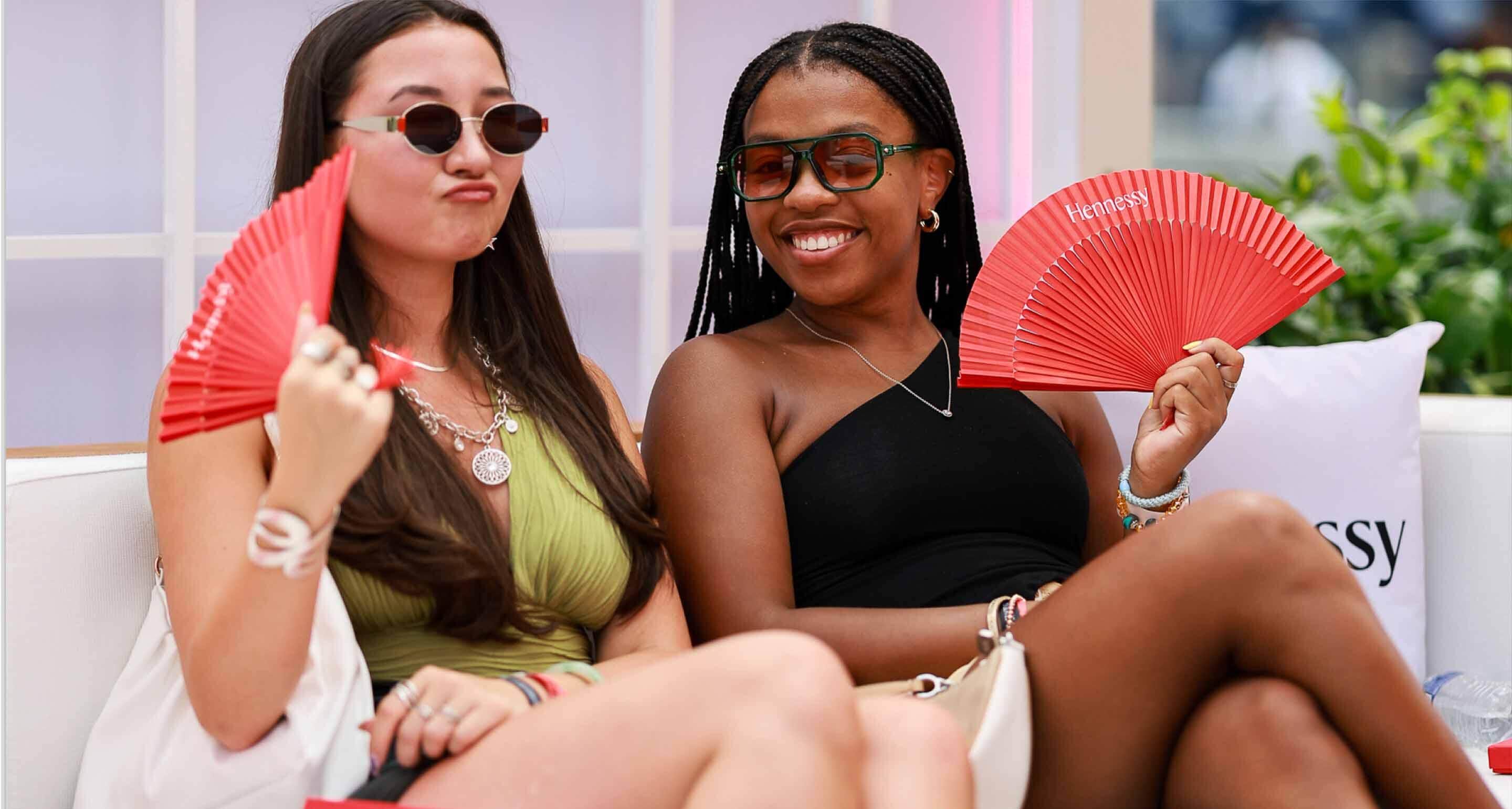 Two customers laughing and relaxing in the plush Hennessy lounge during exclusive brand experiences.