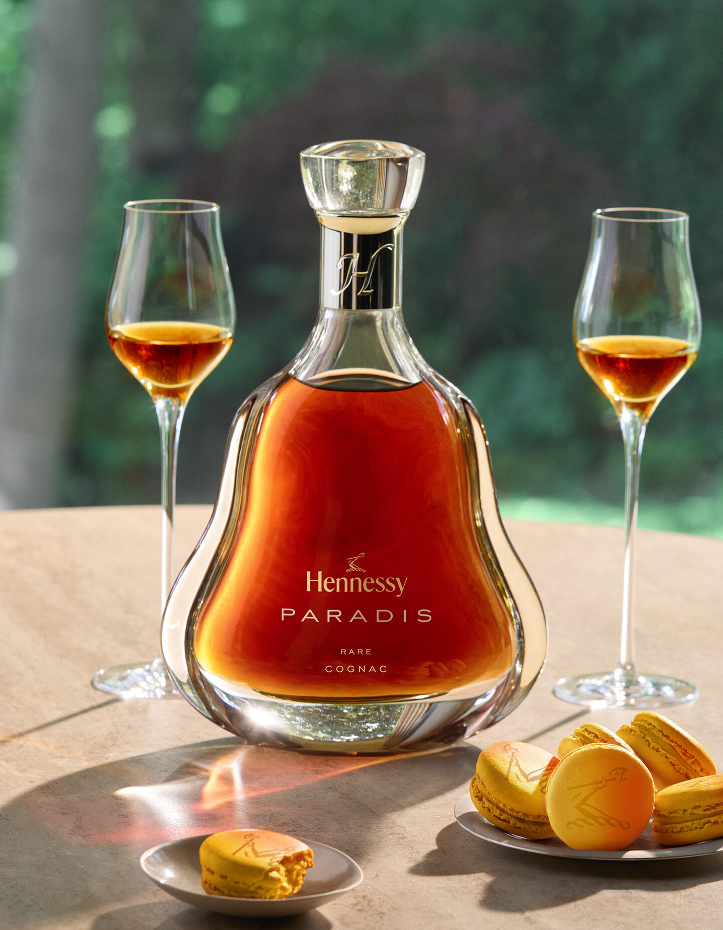 A decanter of Hennessy Paradis upgrade on a table, next to 2 glasses of cognac and a plate of passionfruit macarons