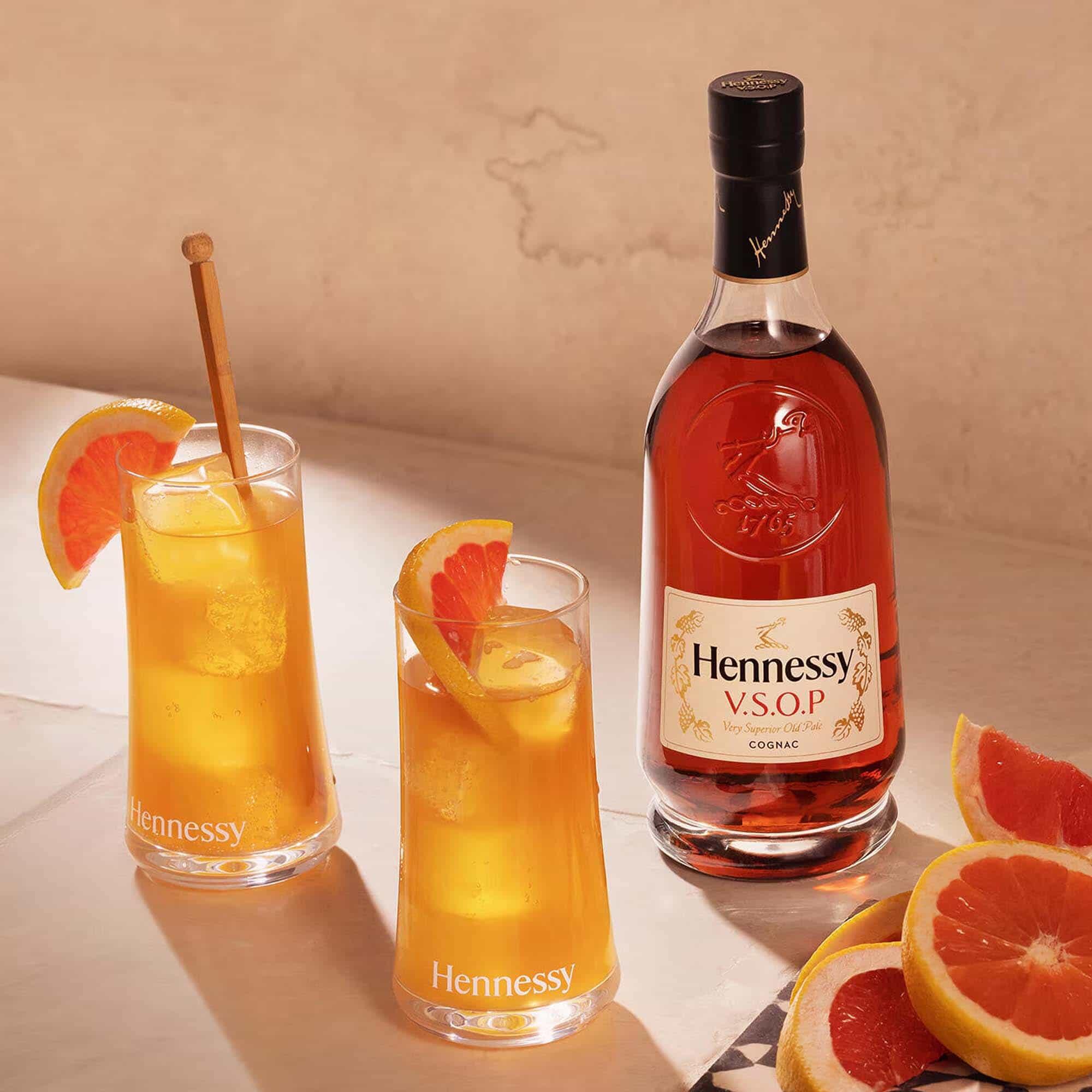 Sparkling Hennessy V.S.O.P bottle with two golden cocktails beside fresh grapefruit wedges.