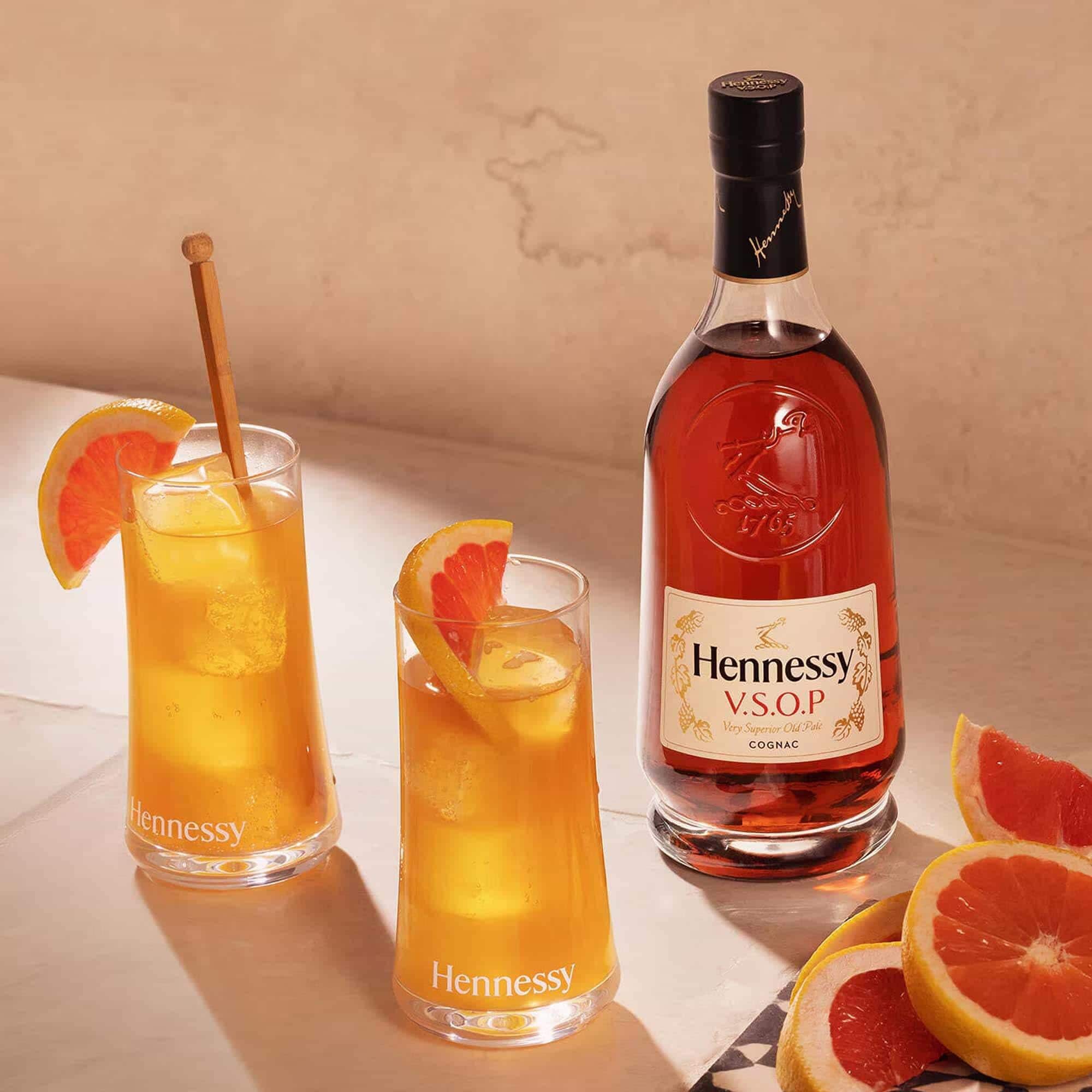 Sparkling Hennessy V.S.O.P bottle with two golden cocktails beside fresh grapefruit wedges.
