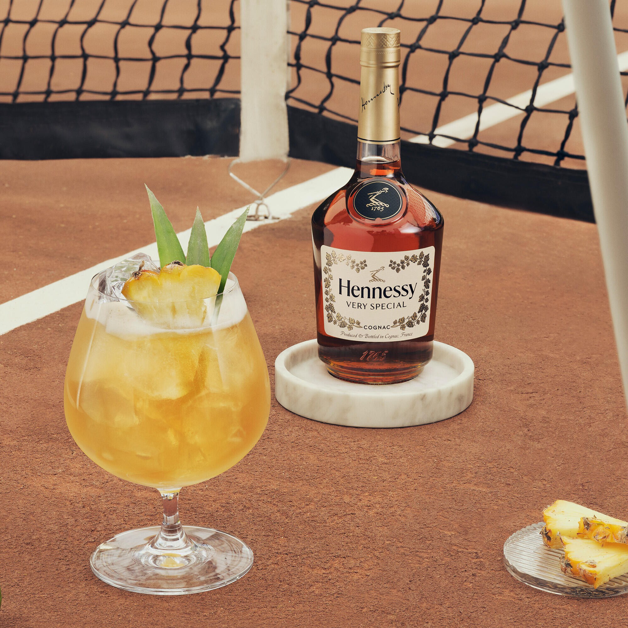 Hennessy V.S. bottle beside an enticing cocktail with pineapple slices for garnish.