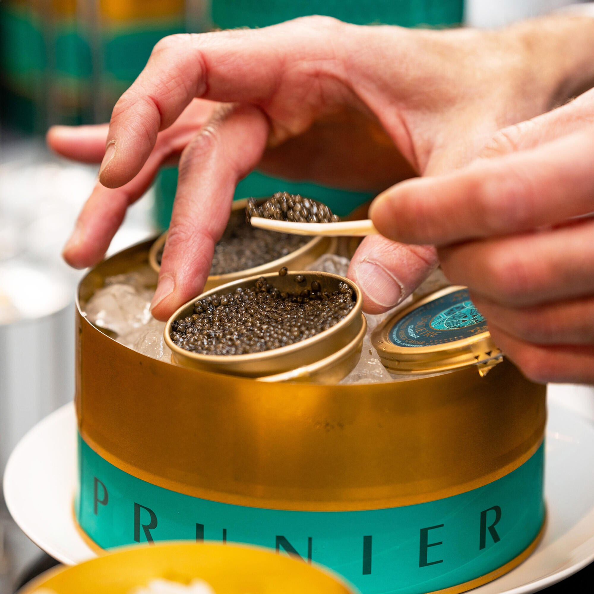 Close-up of a a guest's hand holding a mother-of-pearl spoon, as they are helping themselves to a serving of Prunier Oscietra caviar