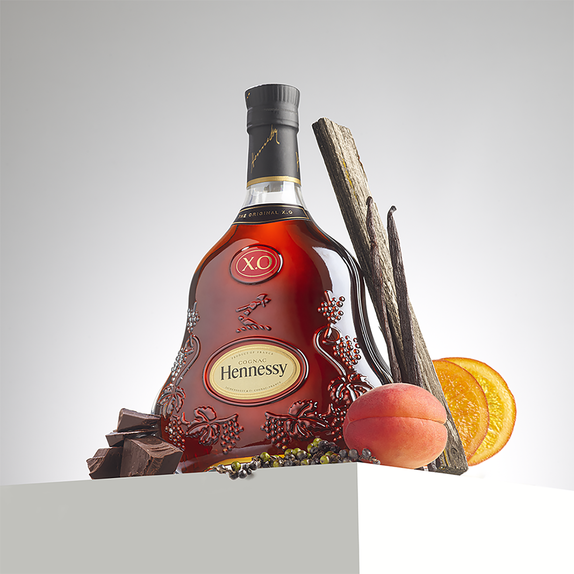 Bottle of Hennessy X.O surrounded by fruits and spices illustrating its main aromatic notes (such as apricot, dried orange, vanilla, oak, chocolate)
